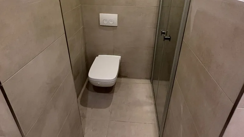 Wand-WC in einem schmalen, großformatig gefliesten WC-Raum mit Glastür