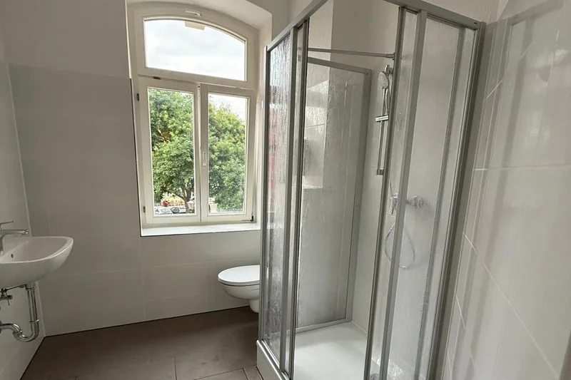 Günstig saniertes Altbaubad mit weißen Fliesen, Duschkabine und Bogenfenster